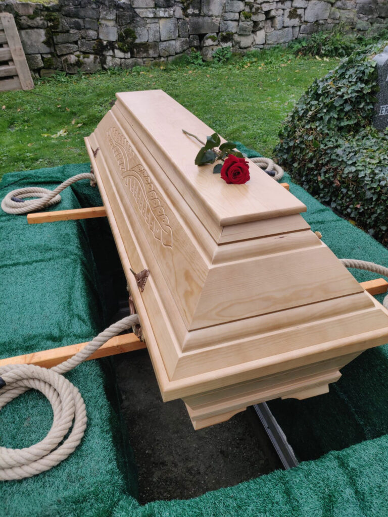 Albatros-Bestattungen® Hölzerner Sarg mit einzelner Rose, bereit in die Erde gelassen zu werden.