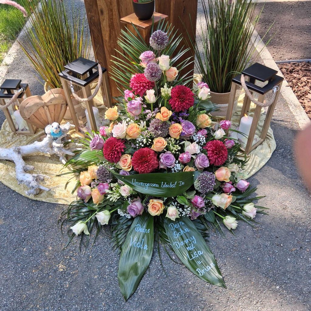 Albatros-Bestattungen® Blumengesteck aus verschieden farbigen Blumen, mit einem "Unvergessen bleibst du" Schild.